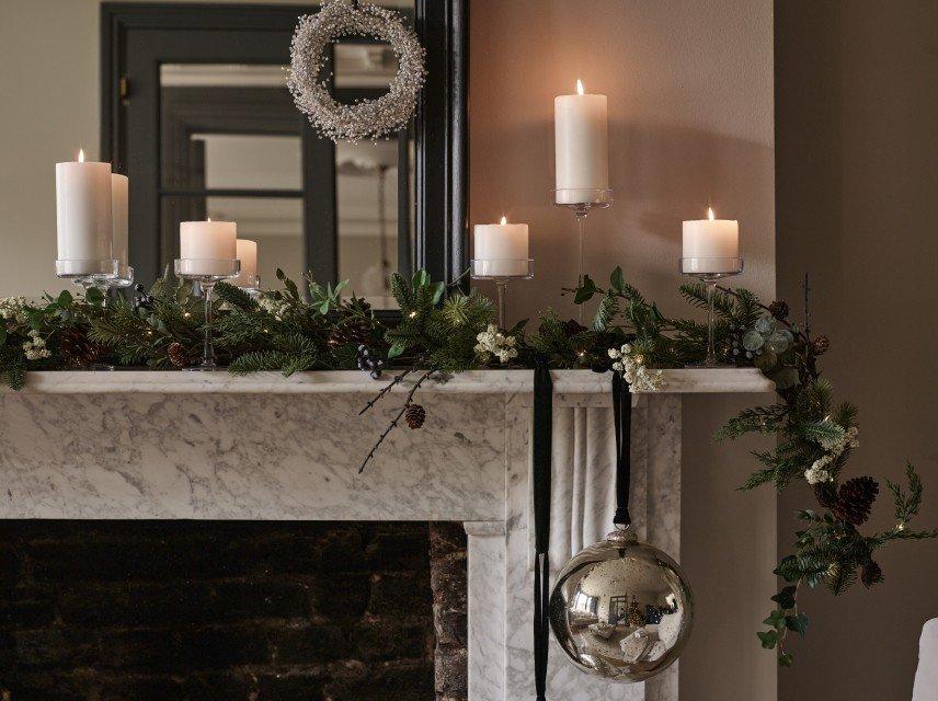 a mantle with candles, greenery and a mirror with a candle on it