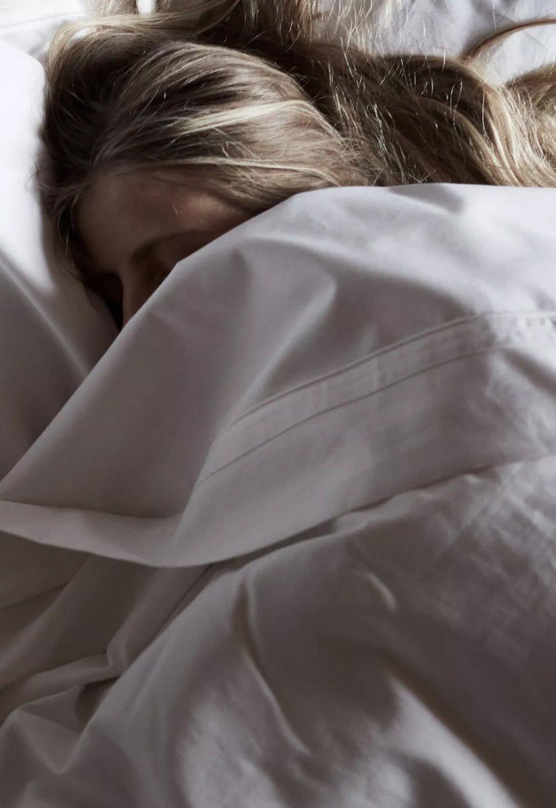 a woman sleeping in a bed with a white comforter