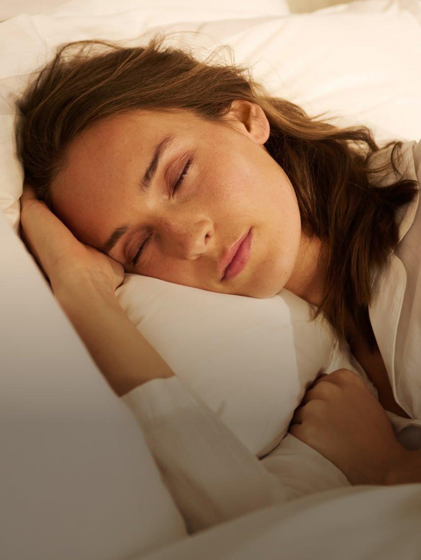 a woman sleeping in a bed with a white sheet