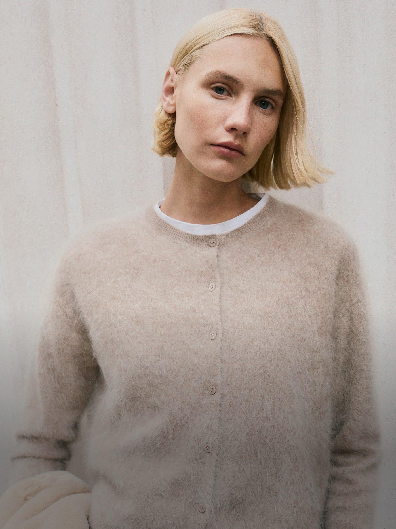 a woman in a beige sweater and white jacket posing for a picture
