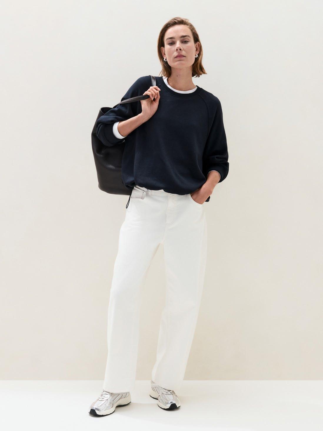 a woman in a black sweater and white pants holding a bag
