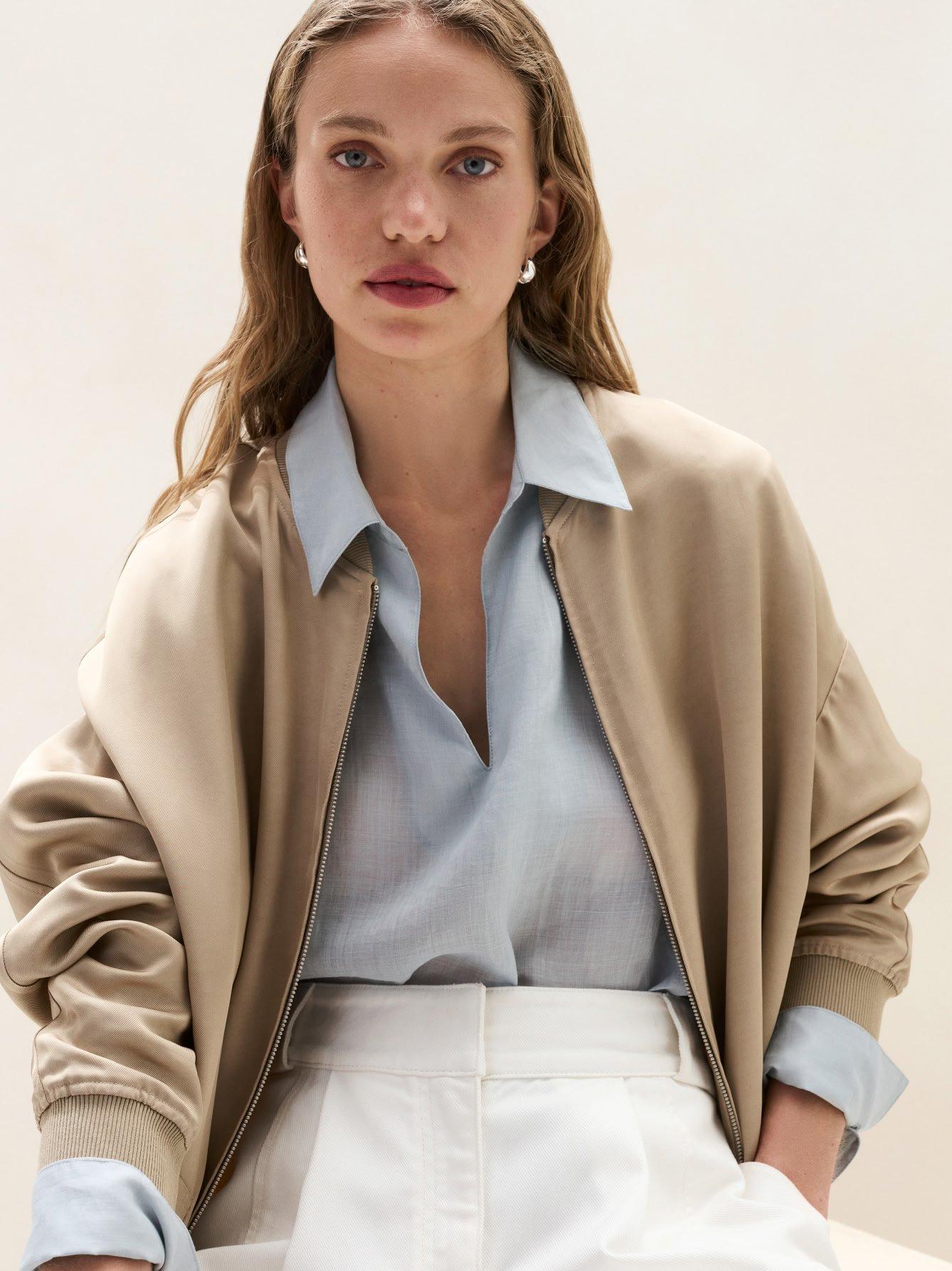a woman in a blue shirt and beige jacket sitting on a chair