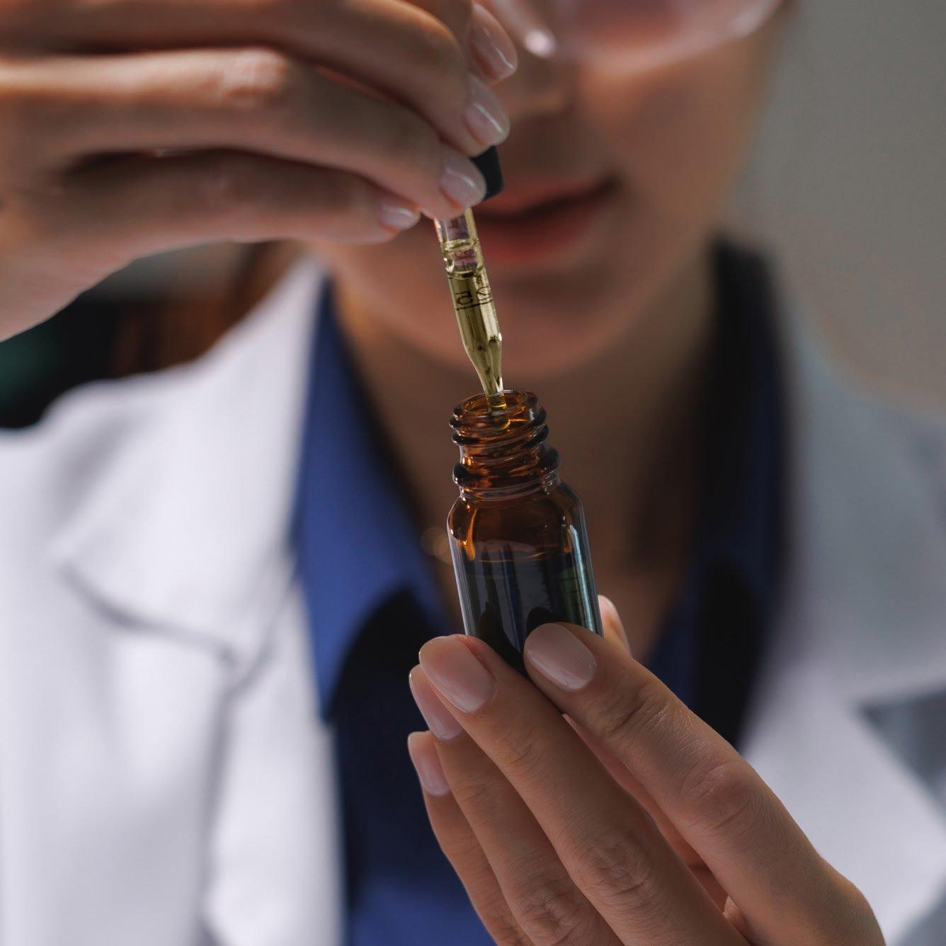a woman in lab coat holding a bottle of liquid with a dropper