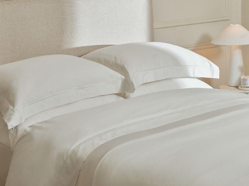 a bed with white sheets and pillows in a bedroom