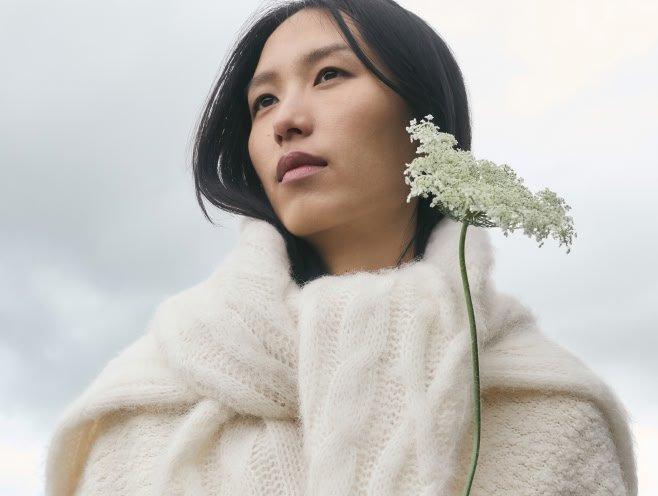 a woman in a white sweater holding a flower in her hand