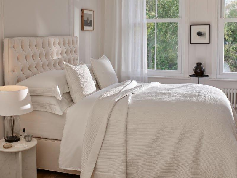 a white bed with a white comforter and pillows in a bedroom