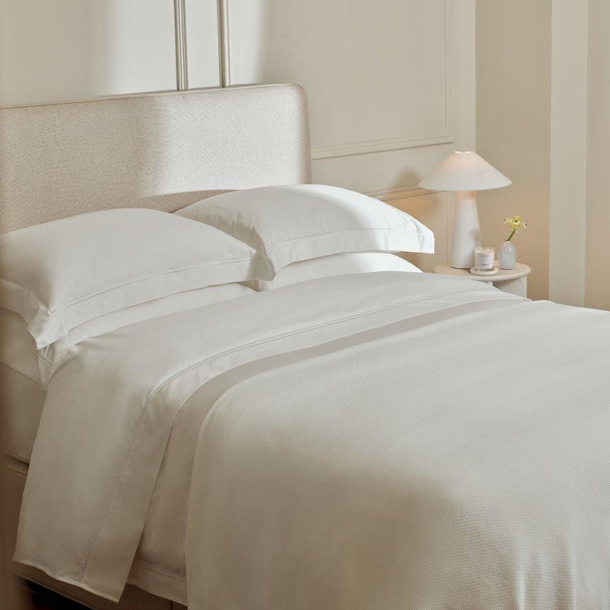 a bed with white sheets and pillows in a bedroom