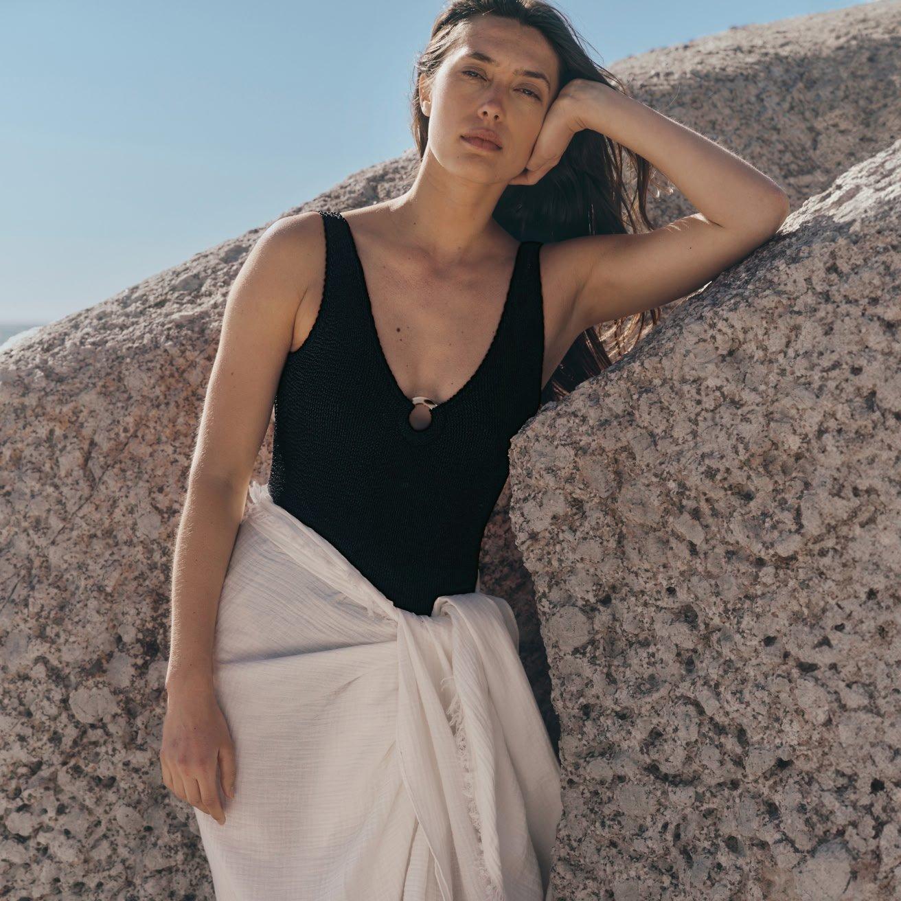 a woman in a black and white dress leaning against a rock
