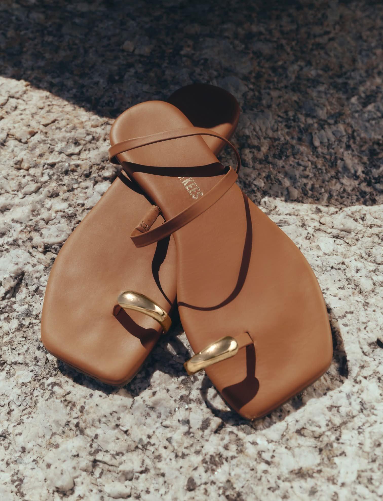 a pair of tan sandals with gold buckles on a rock