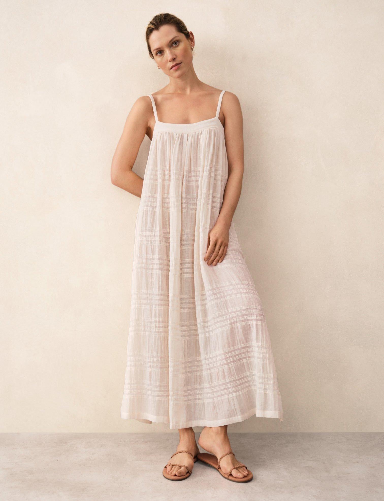 a woman in a white dress stands against a wall