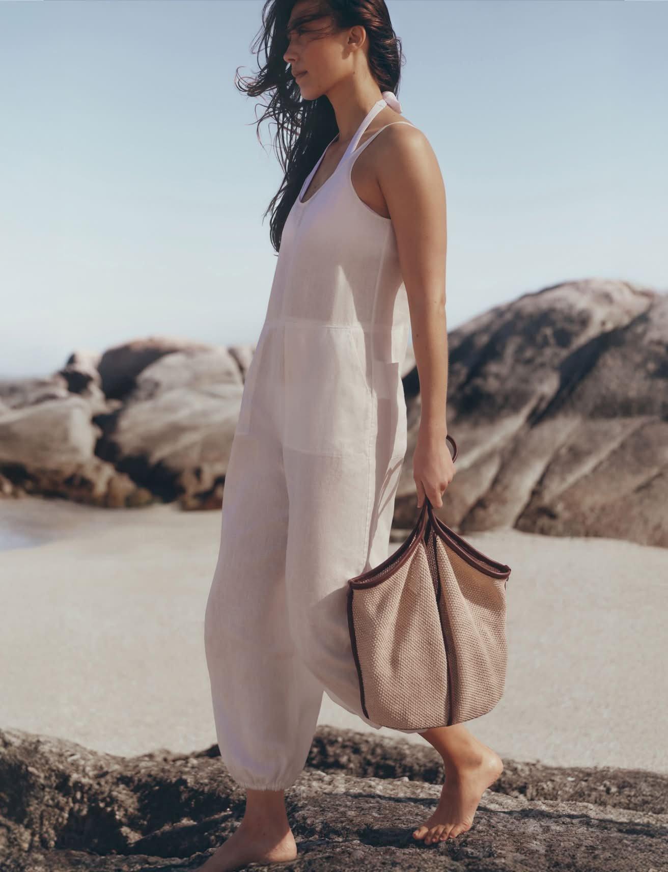 a woman walking on a beach carrying a bag