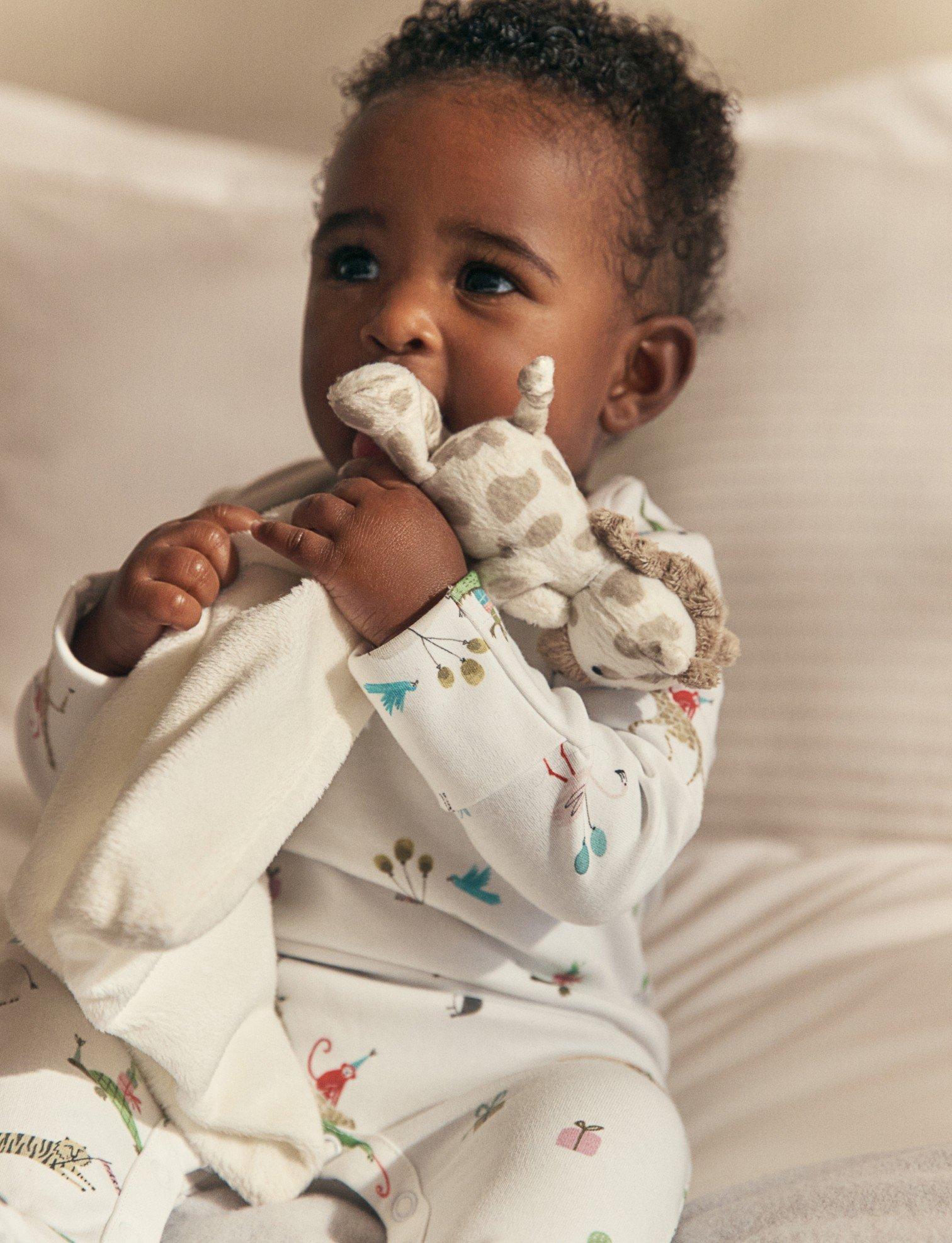 a baby in pajamas holding a stuffed animal on a bed