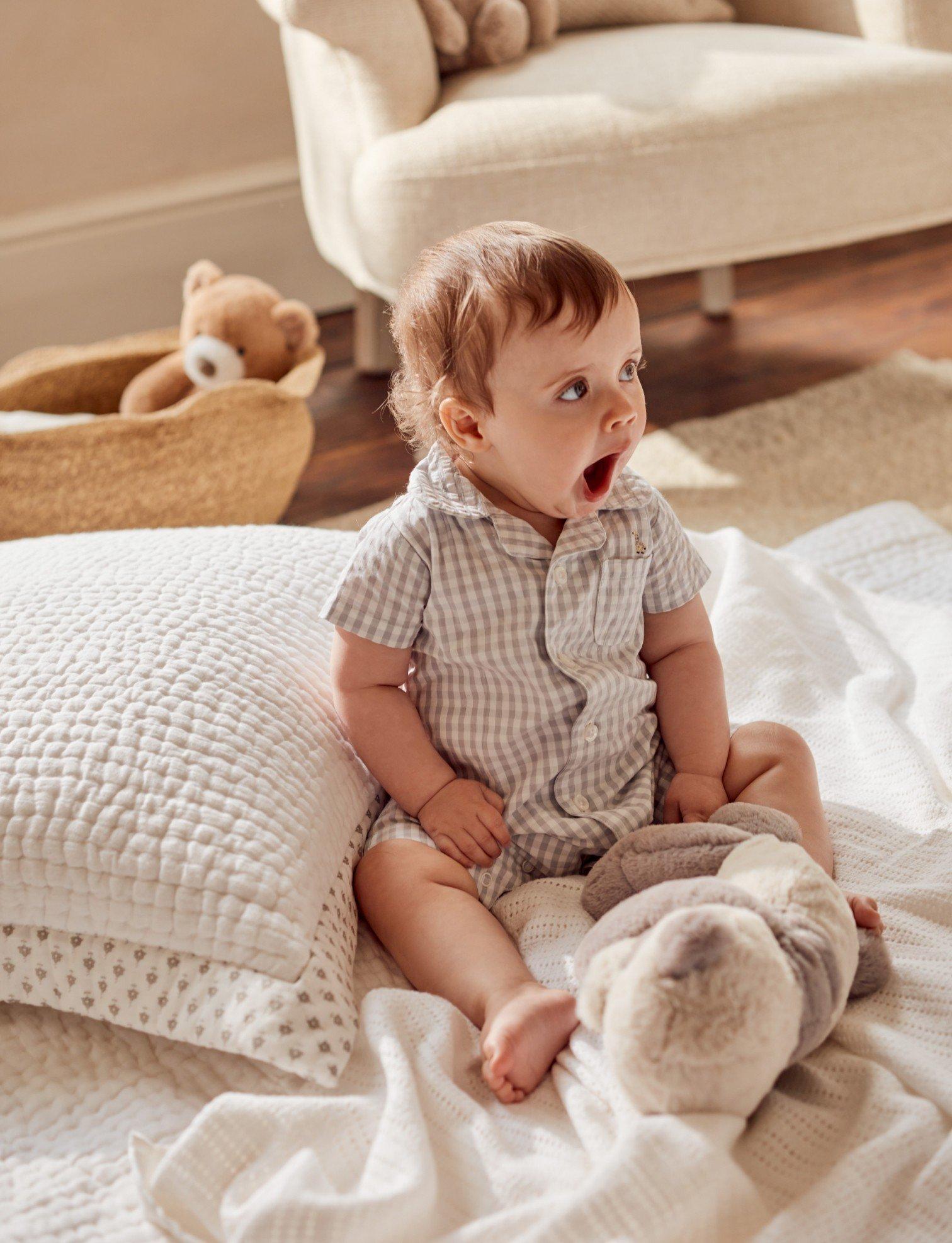 a baby sitting on a bed with a teddy bear