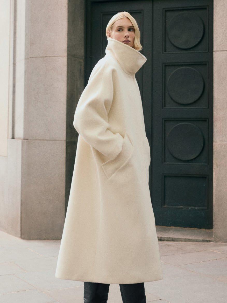 a woman in a long white coat standing in front of a building