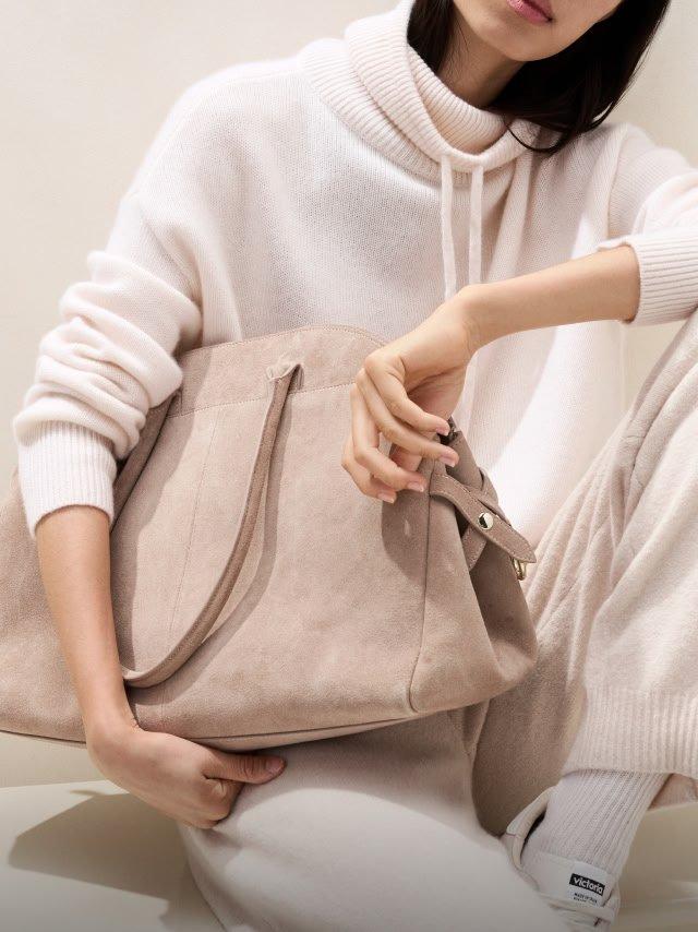 a woman in a white sweater holding a bag on her lap