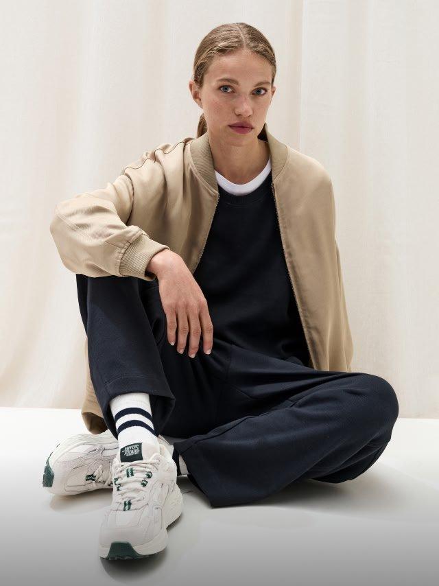 a man sitting on the floor wearing a jacket and sneakers