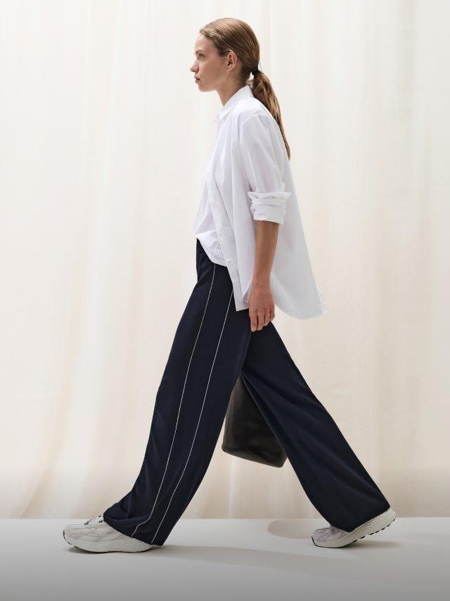 a woman walking down a runway in a white shirt and black pants