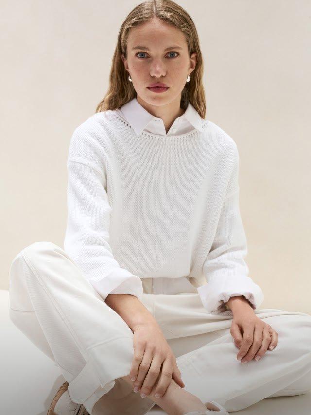 a woman in a white sweater sitting on the floor