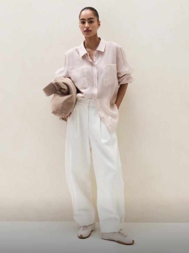 a woman in a pink shirt and white pants standing against a wall