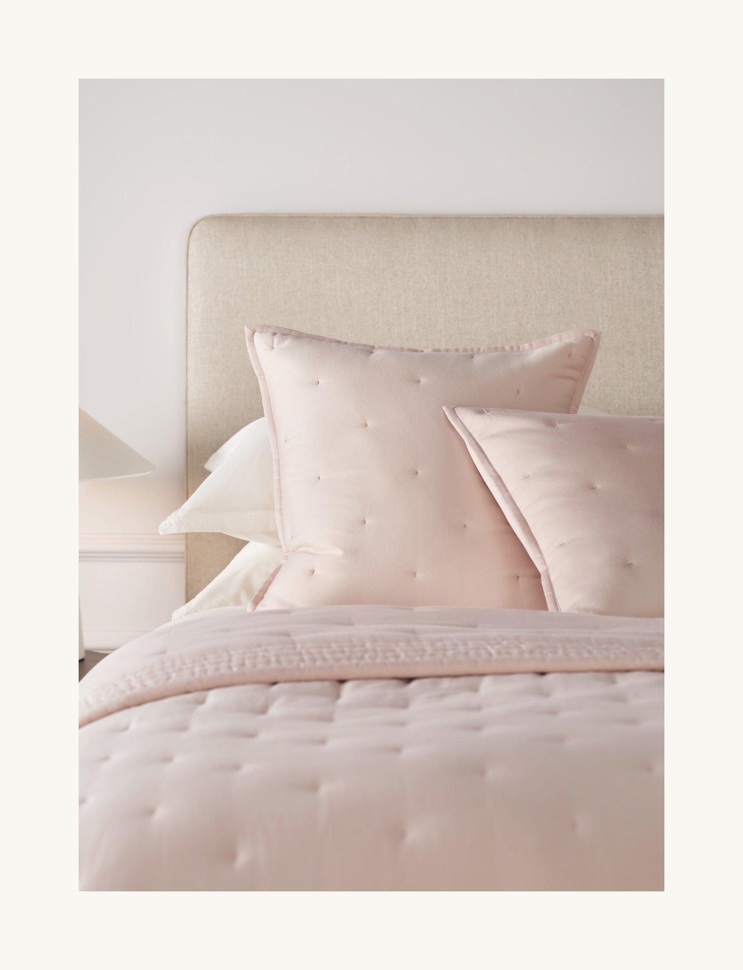 a bed with a pink comforter and pillows on it