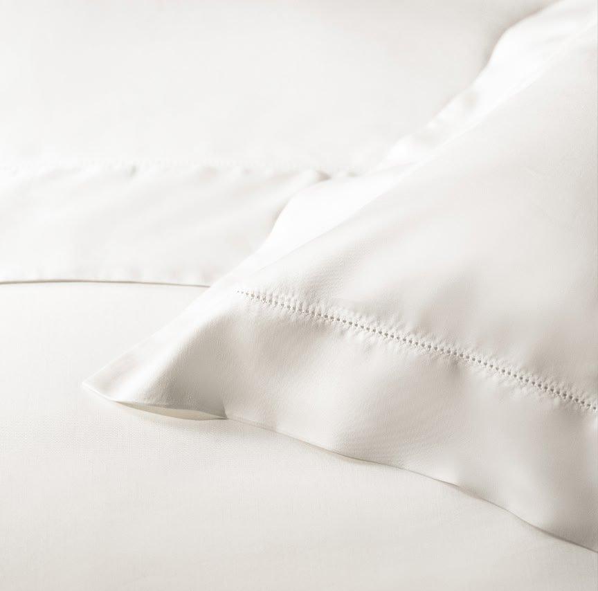 a close up of a white bed with pillows and sheets