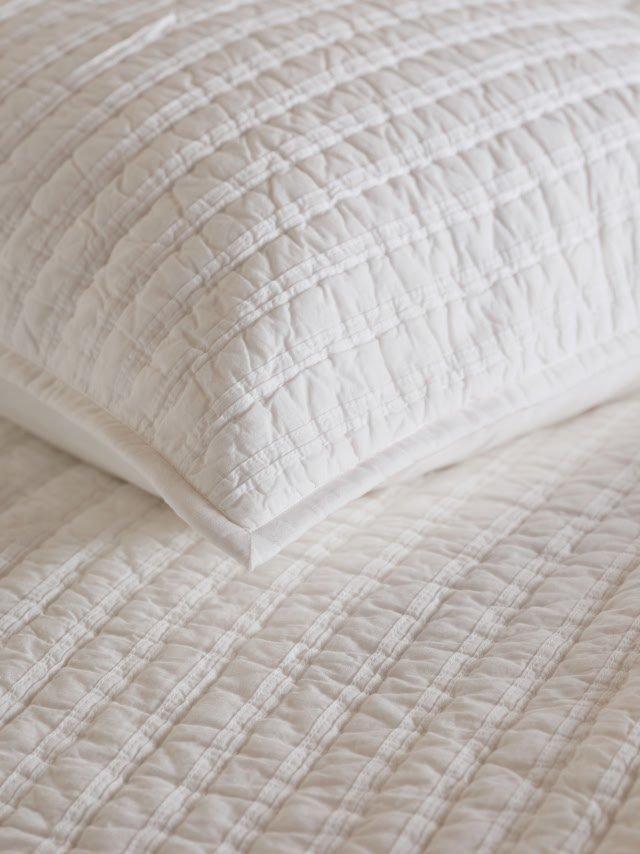 a close up of a white pillow on a bed with a white sheet