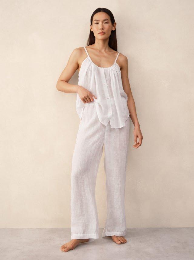 a woman in white pajamas stands against a wall