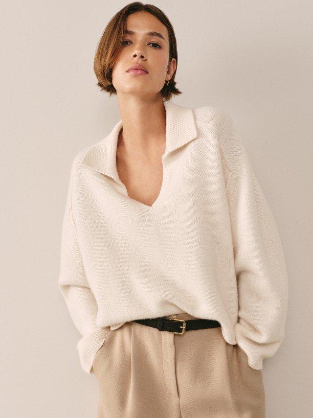 a woman in a white sweater and tan pants with a yellow dot on her sweater