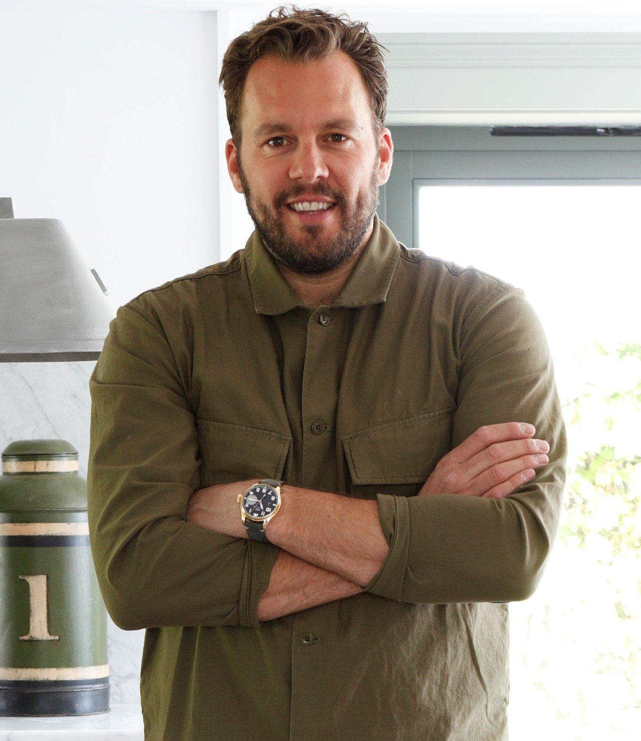 a man with a watch and a green shirt standing in a kitchen