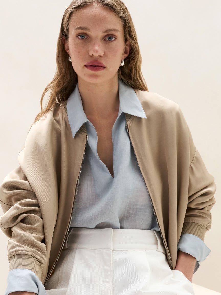 a woman in a blue shirt and beige jacket sitting on a chair