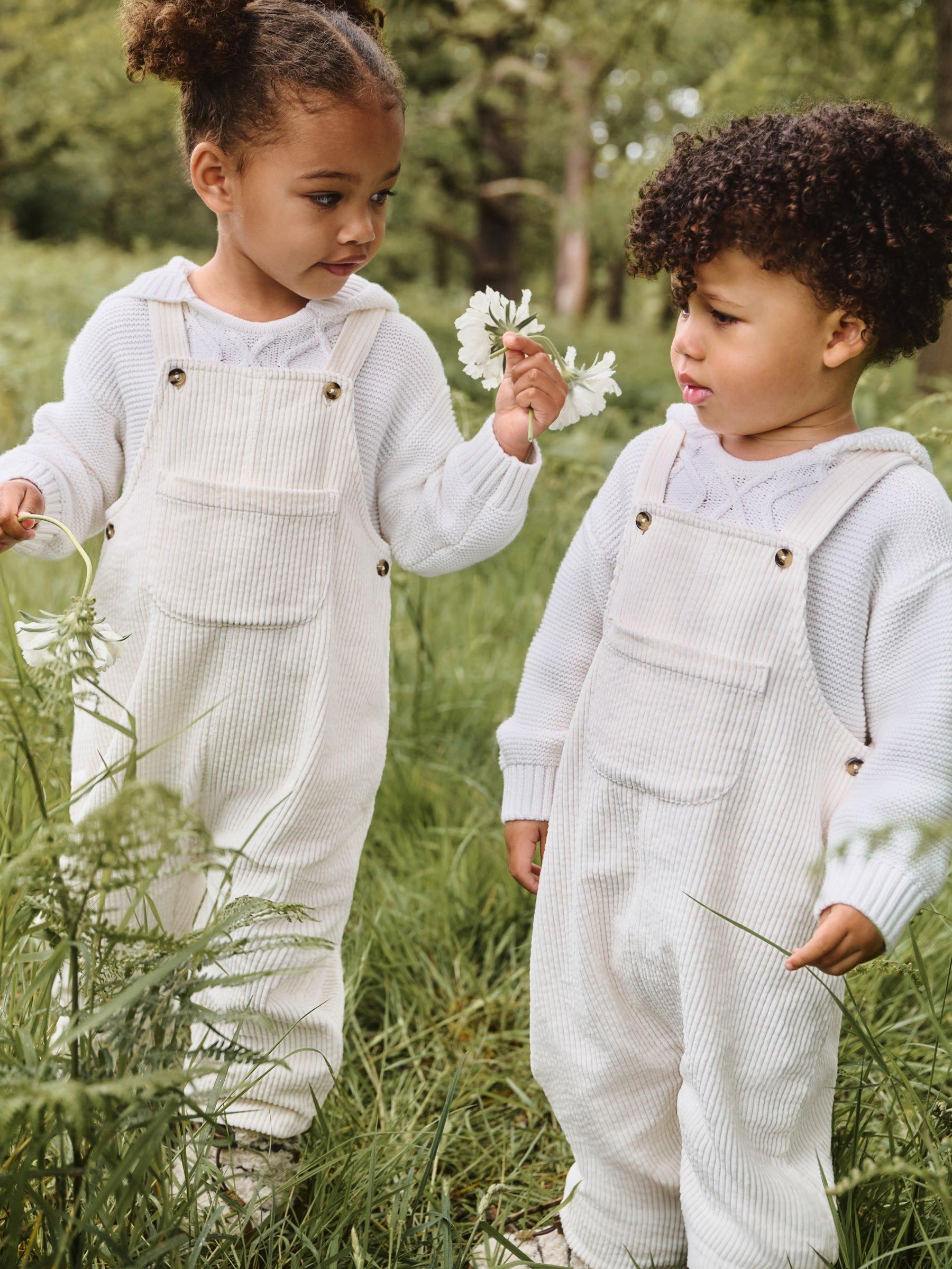 a boy and a girl in white outfits picking flowers