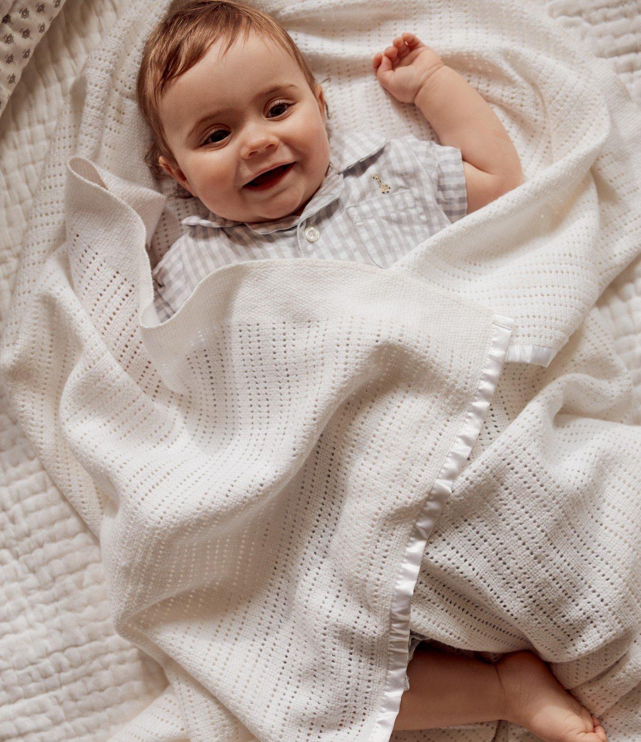 a baby laying on a bed wearing a white and grey dress