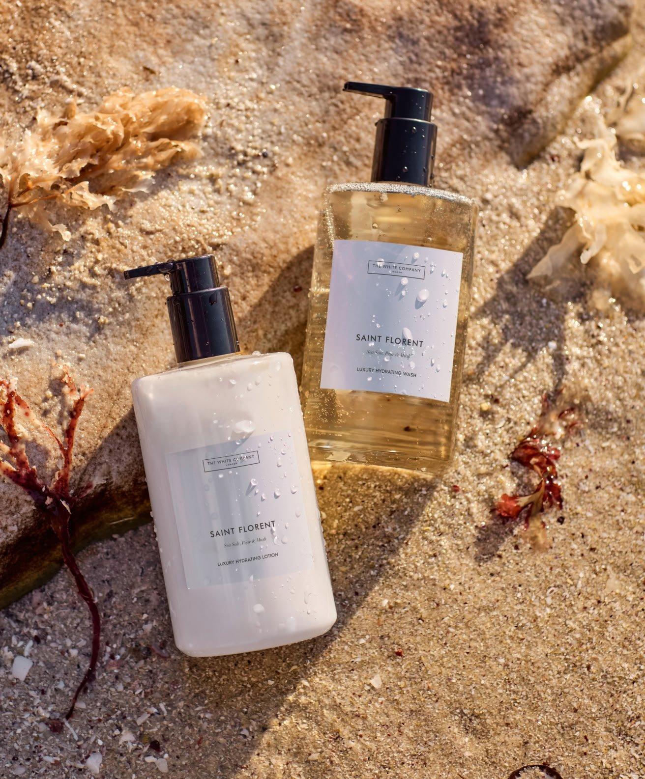 two bottles of soap sitting on a beach next to shells