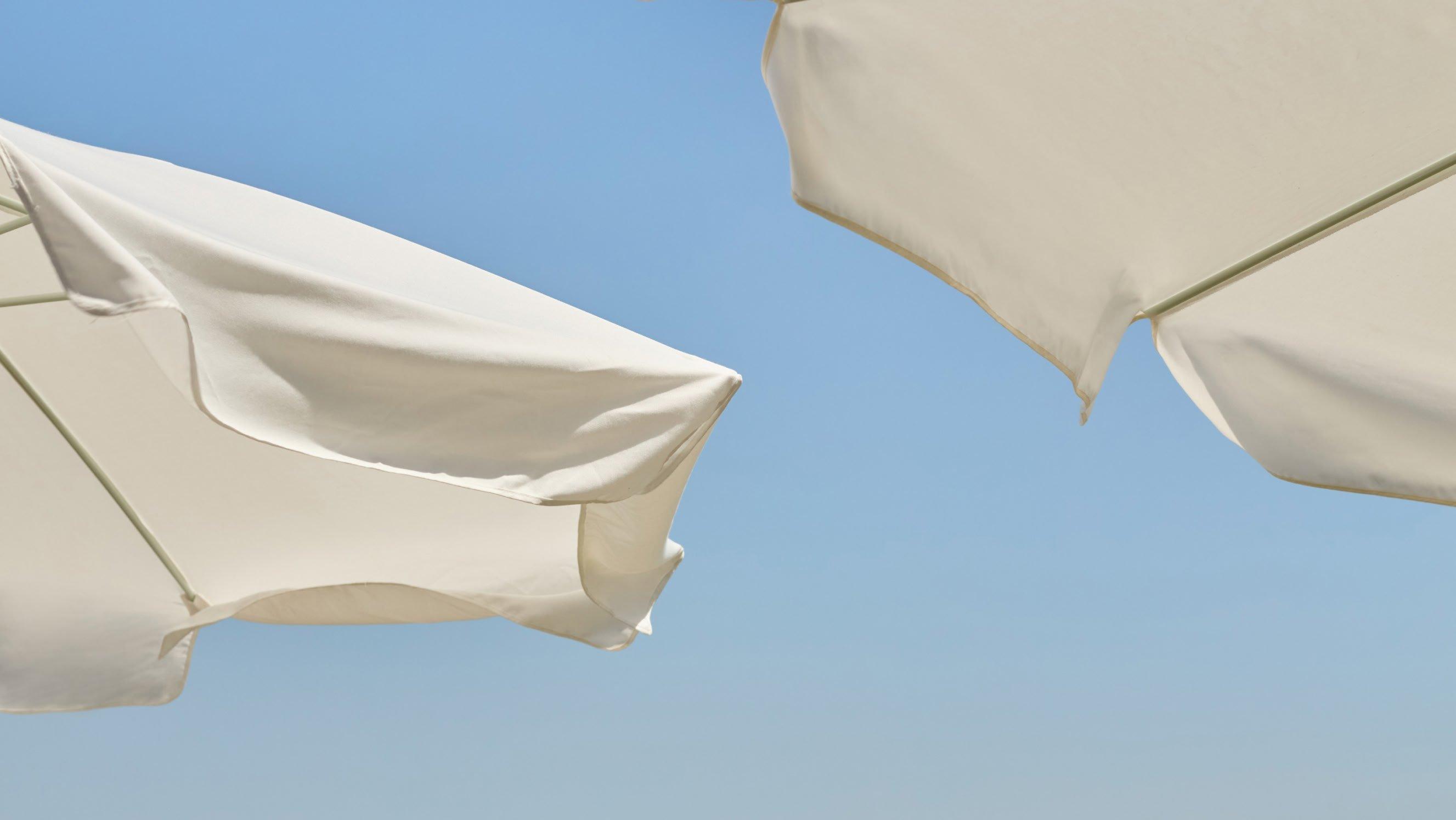 two white umbrellas are open on a beach with a blue sky