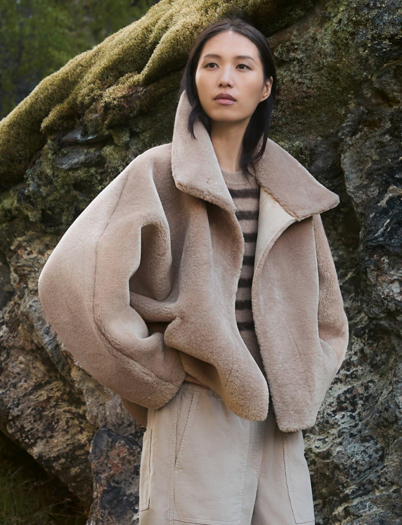 a woman in a beige jacket standing next to a rock