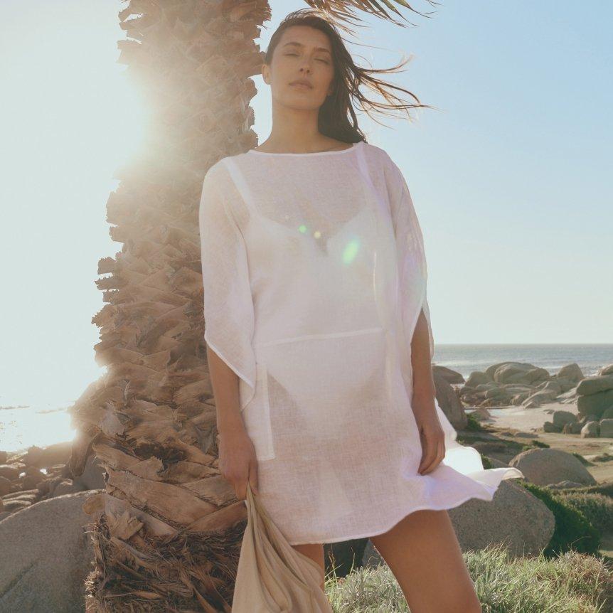 a woman in white dress standing next to palm tree on beach