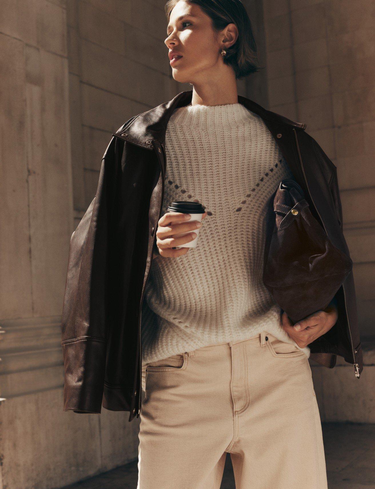 a woman in a brown jacket holding a coffee cup