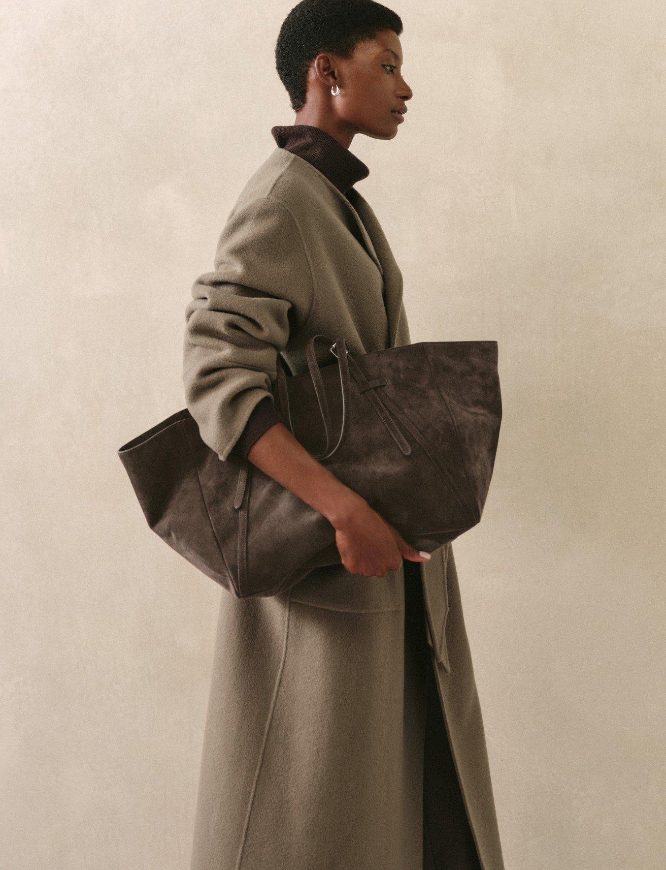 a woman in a long coat holding a large brown bag