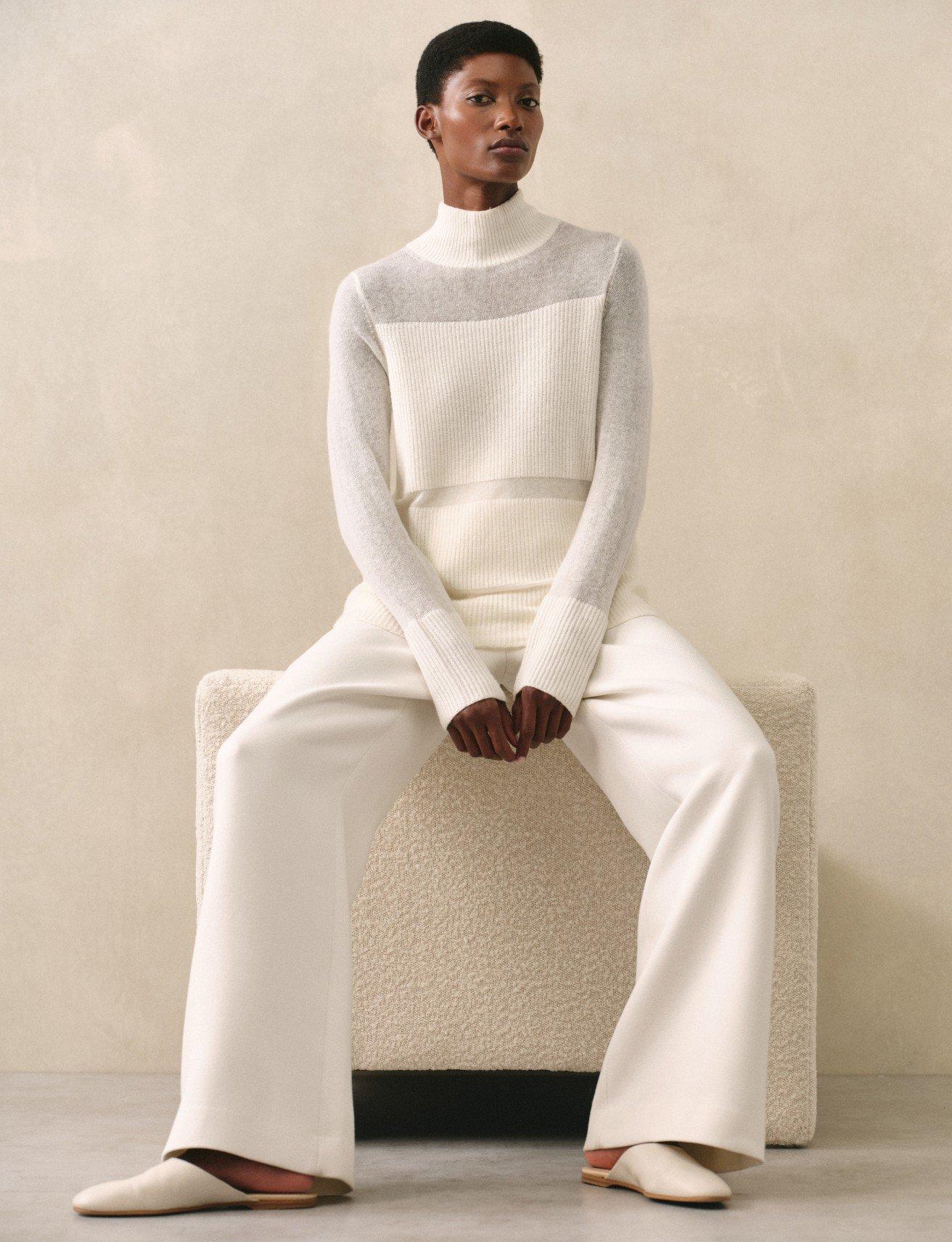 a woman in a white sweater and pants sitting on a stool