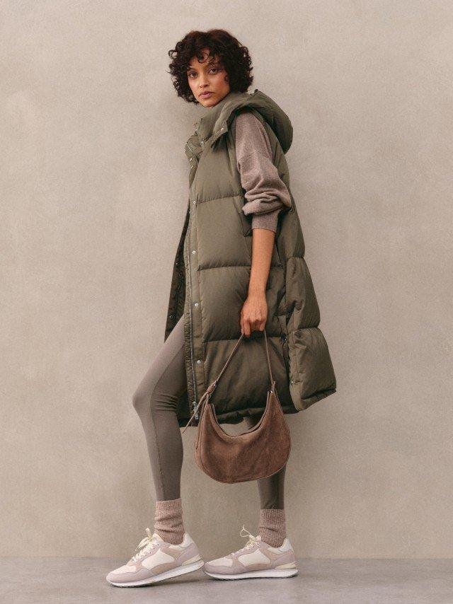 a woman in a puffy vest and leggings holding a purse