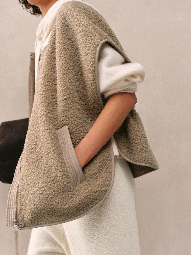 a woman in white pants and a beige jacket holding a black bag