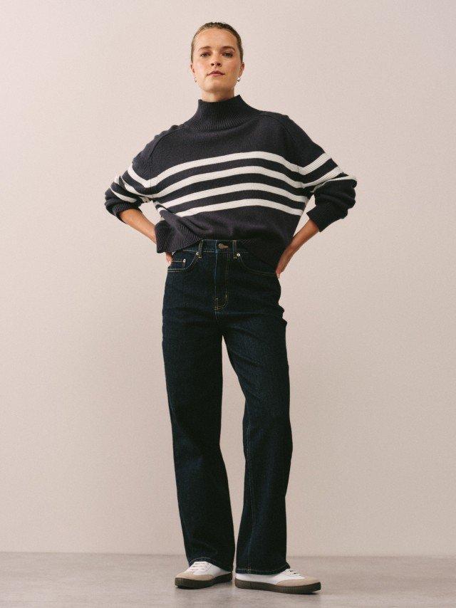 a woman standing in a room wearing a striped sweater and jeans