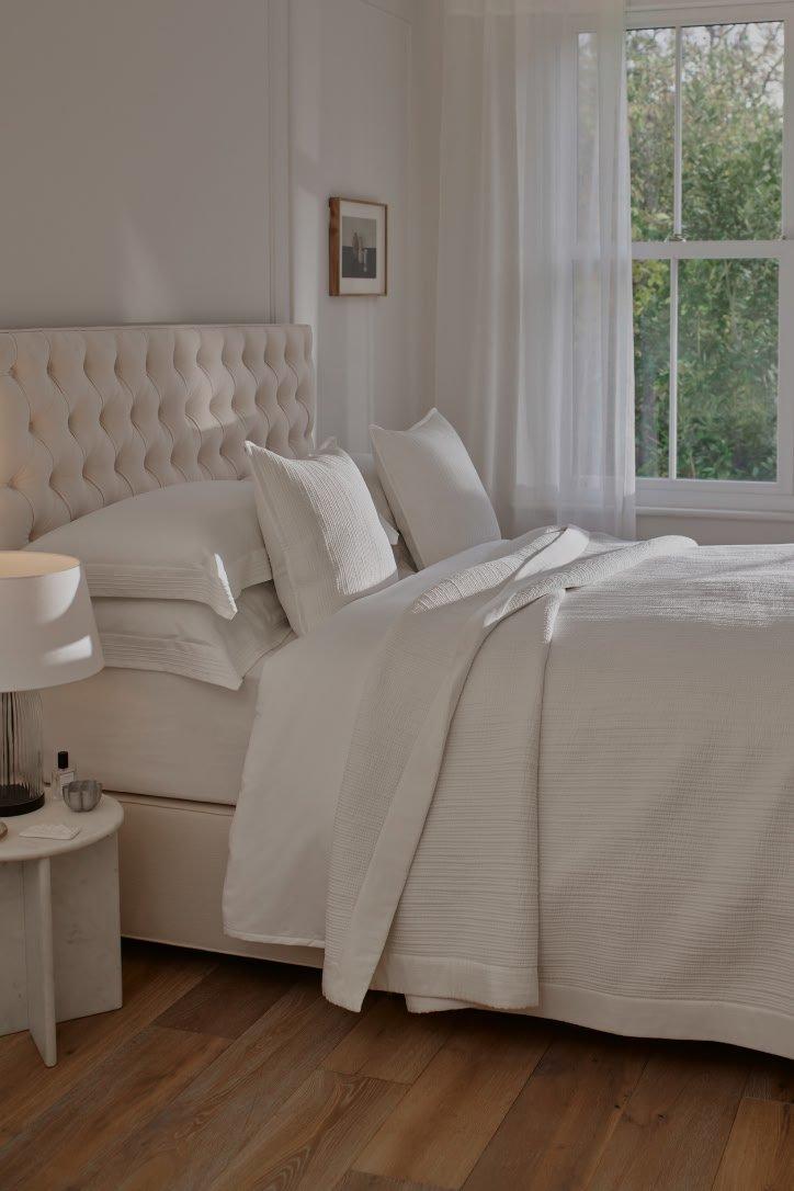 a white bed with white sheets and pillows in a bedroom