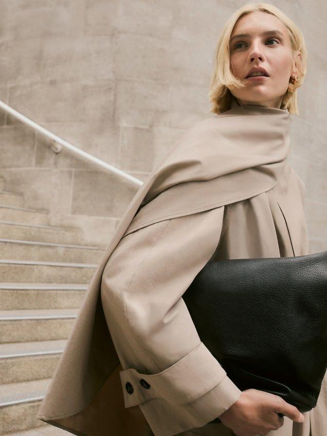 a woman in a beige coat holding a black bag