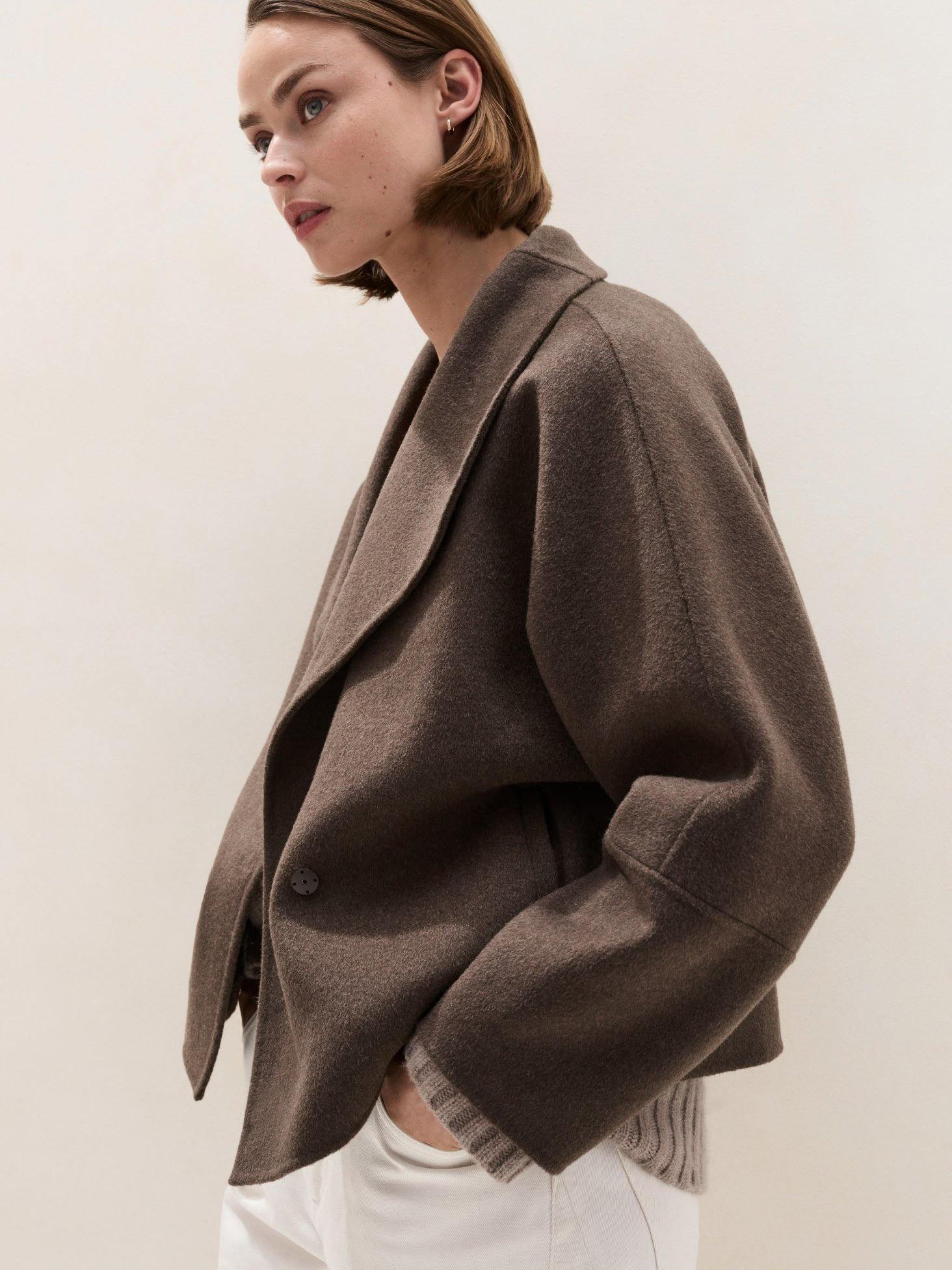 a woman in a brown jacket and white pants standing