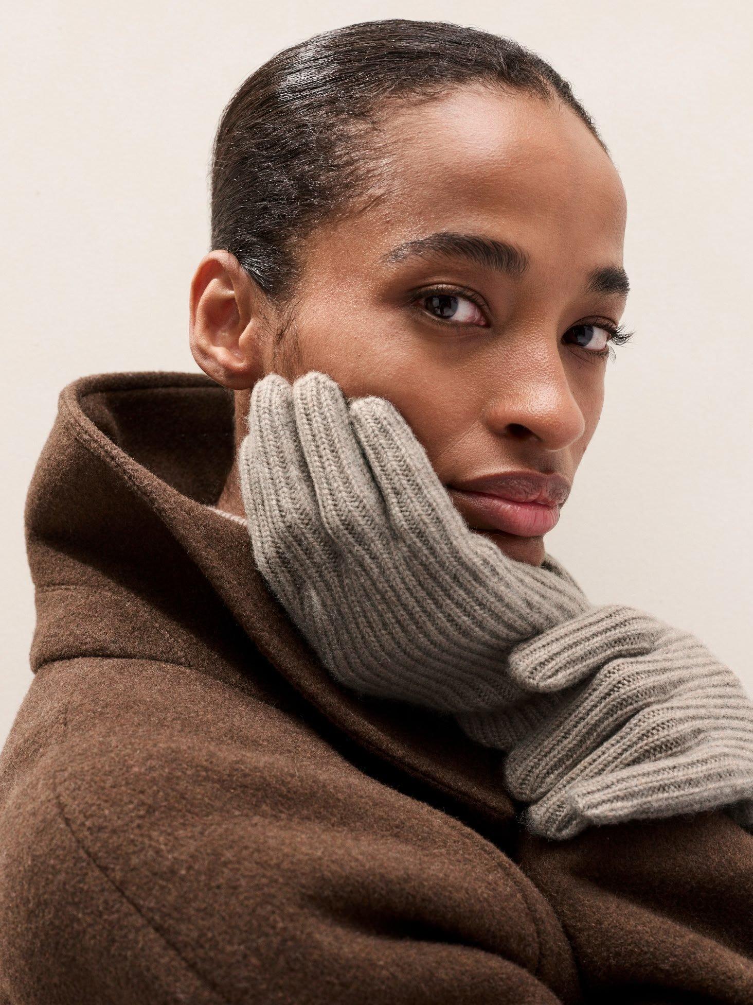 a woman with a brown coat and gloves holding her hand to her face