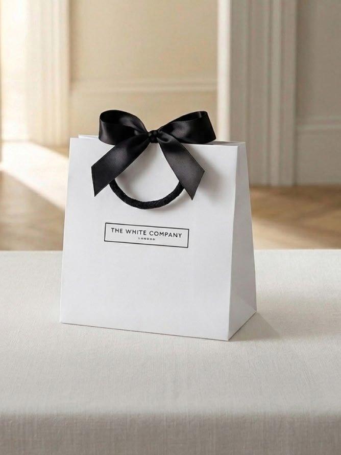 a white paper bag with a black bow sitting on a table