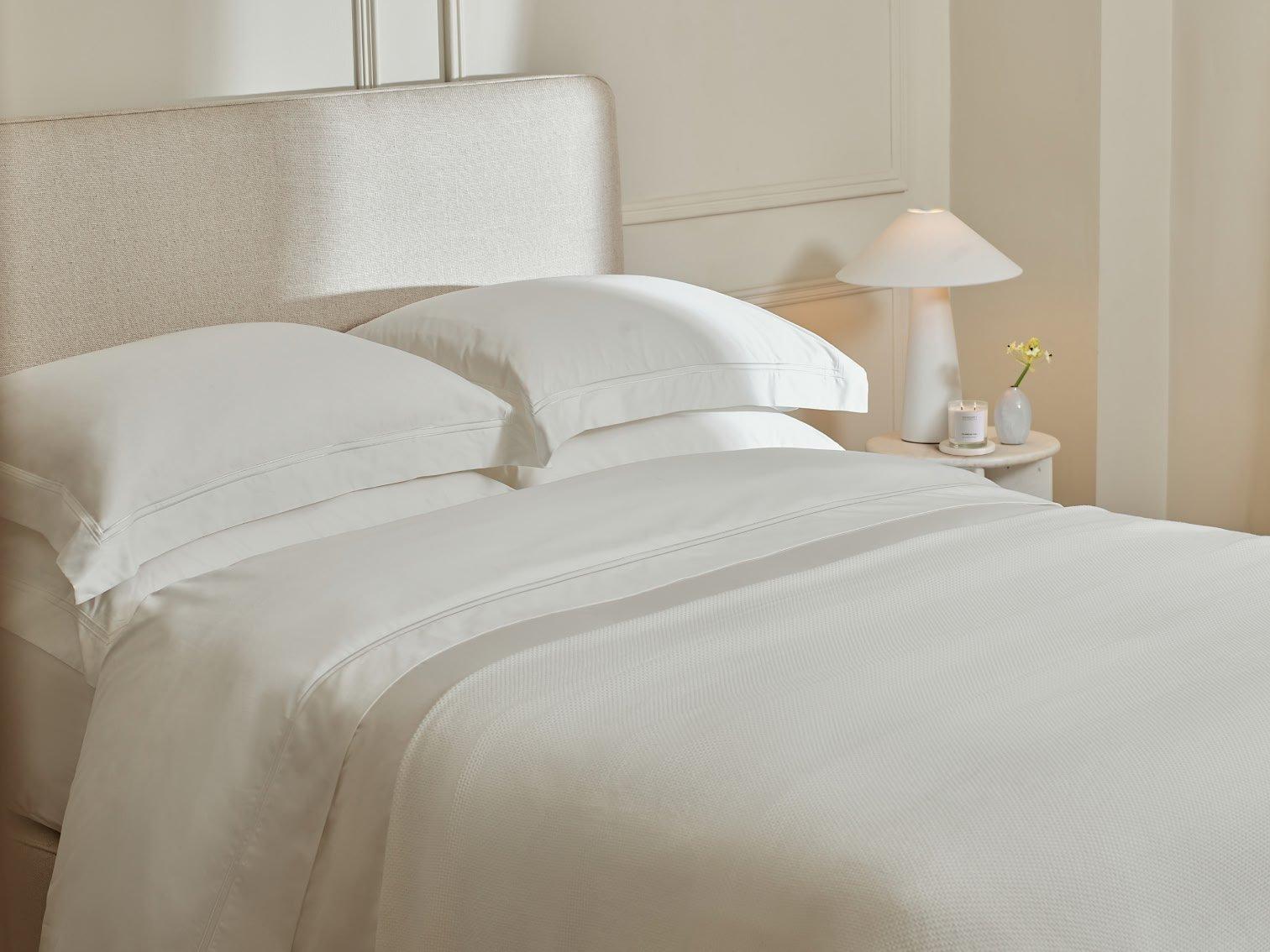 a bed with white sheets and pillows in a bedroom