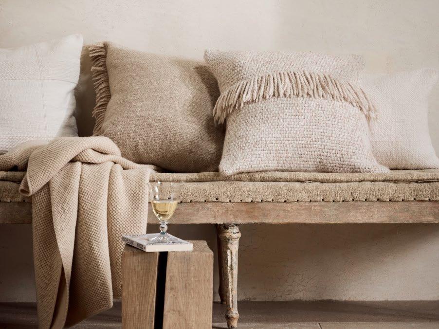 a bench with pillows and blankets on it next to a wine glass