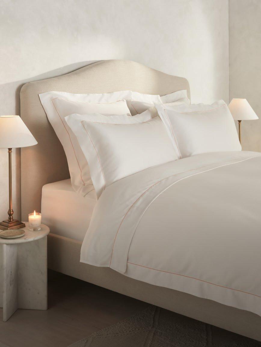 a bed with white sheets and pillows and a yellow lamp